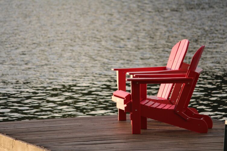 red wooden lounge chair on brown boardwalk near body of water during daytime